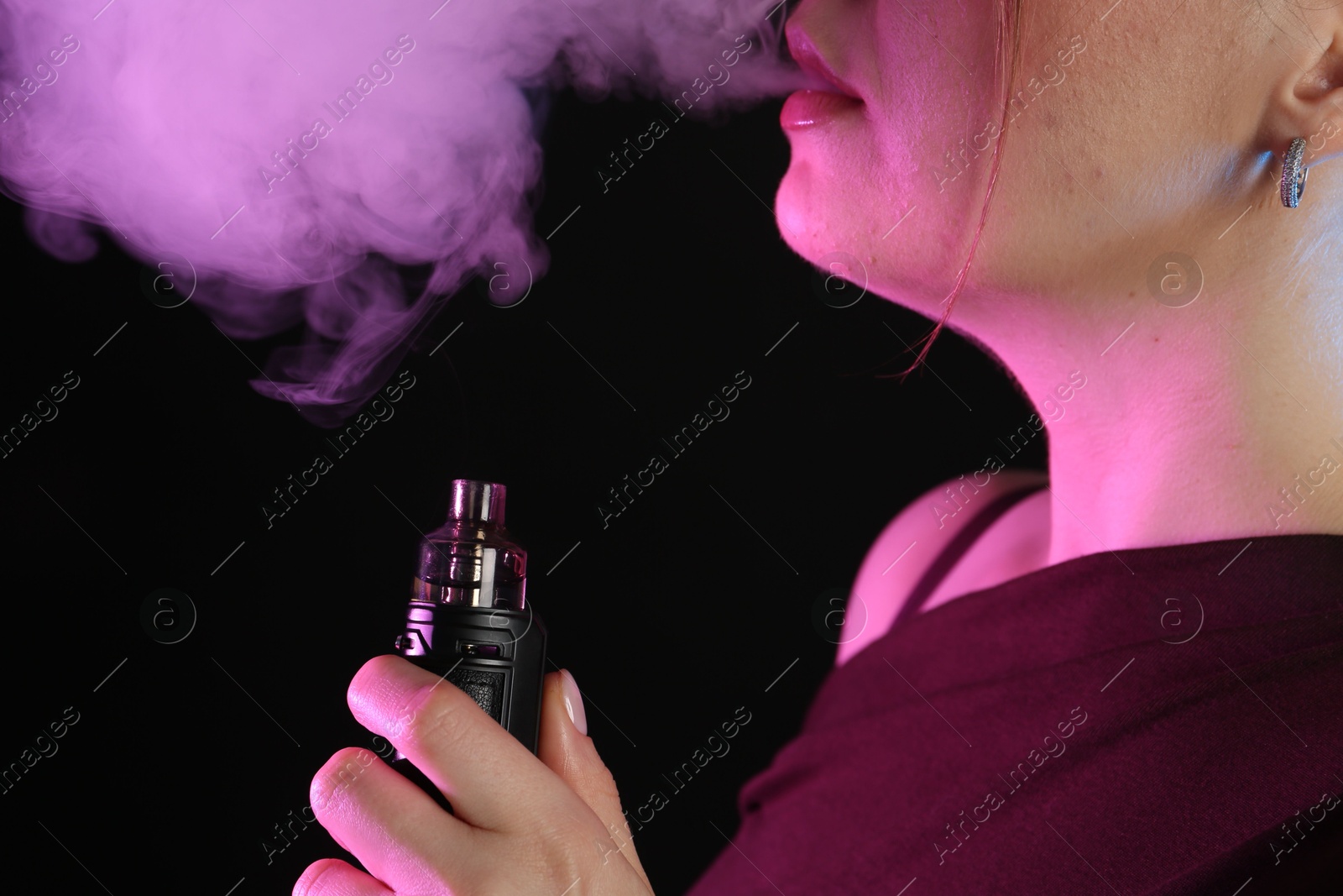 Woman using electronic smoking device in neon lights on black background, closeup Photo of Woman using electronic smoking device in neon lights on black background, closeup