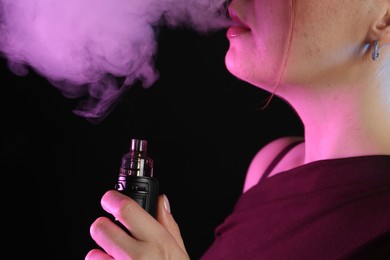 Photo of Woman using electronic smoking device in neon lights on black background, closeup