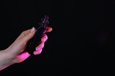 Photo of Woman with electronic smoking device in neon lights on black background, closeup. Space for text