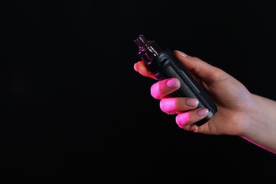 Photo of Woman with electronic smoking device in neon lights on black background, closeup. Space for text