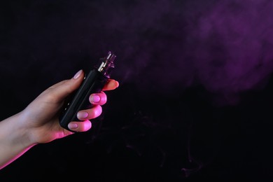 Photo of Woman using electronic smoking device in neon lights on black background, closeup. Space for text
