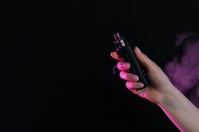 Photo of Woman using electronic smoking device in neon lights on black background, closeup. Space for text