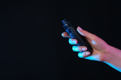 Photo of Woman with electronic smoking device in neon lights on black background, closeup. Space for text