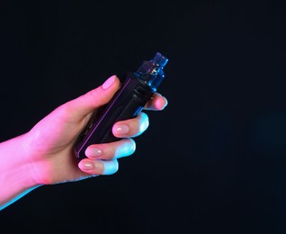 Photo of Woman with electronic smoking device in neon lights on black background, closeup. Space for text