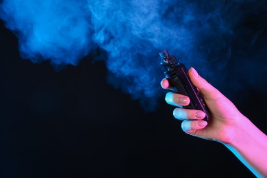 Photo of Woman using electronic smoking device in neon lights on black background, closeup. Space for text