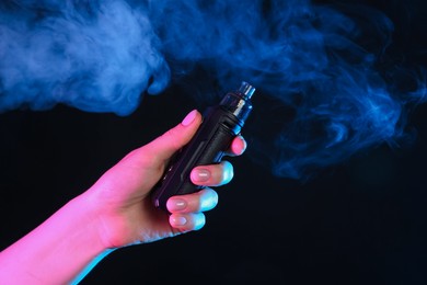 Photo of Woman using electronic smoking device in neon lights on black background, closeup