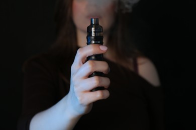 Photo of Woman using electronic smoking device on black background, closeup