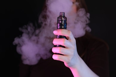 Photo of Woman using electronic smoking device in neon lights on black background, closeup