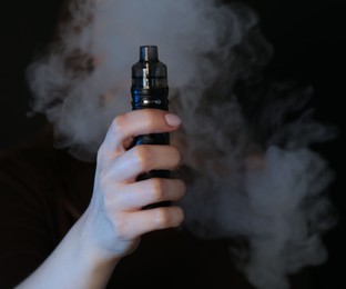 Photo of Woman using electronic smoking device on black background, closeup