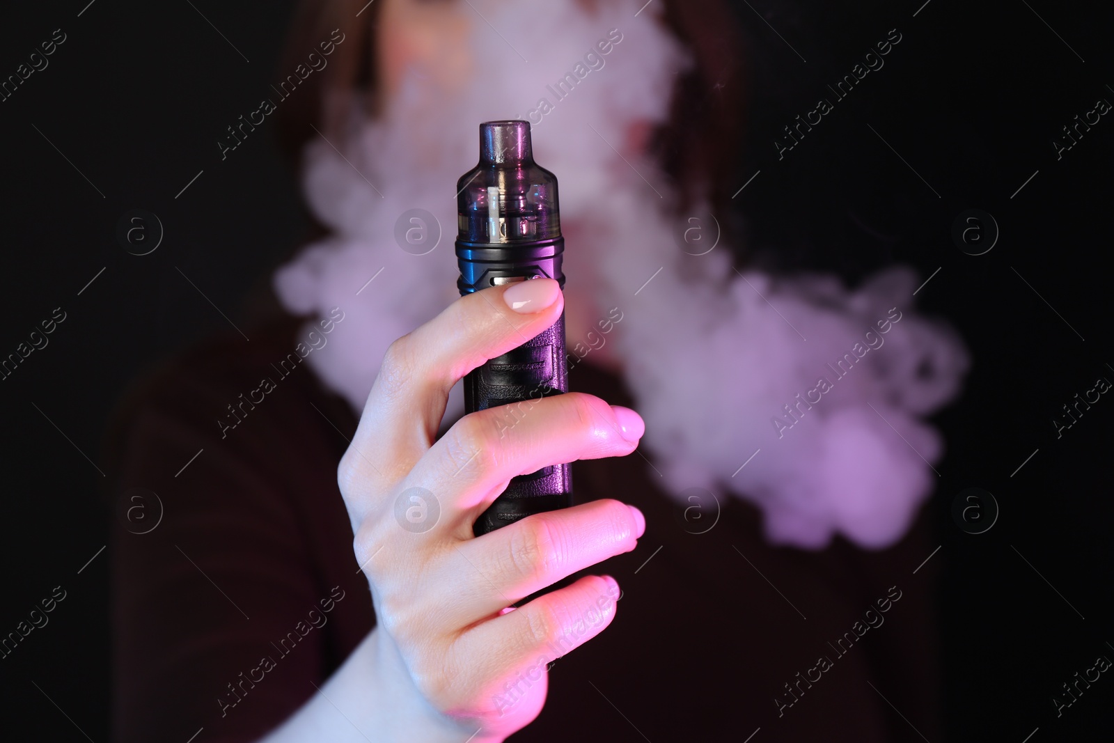 Woman using electronic smoking device in neon lights on black background, closeup Photo of Woman using electronic smoking device in neon lights on black background, closeup