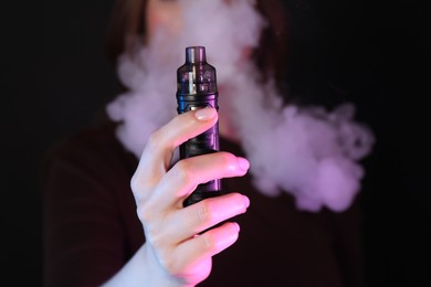 Photo of Woman using electronic smoking device in neon lights on black background, closeup