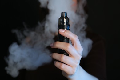 Photo of Woman using electronic smoking device on black background, closeup