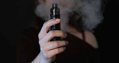 Photo of Woman using electronic smoking device on black background, closeup