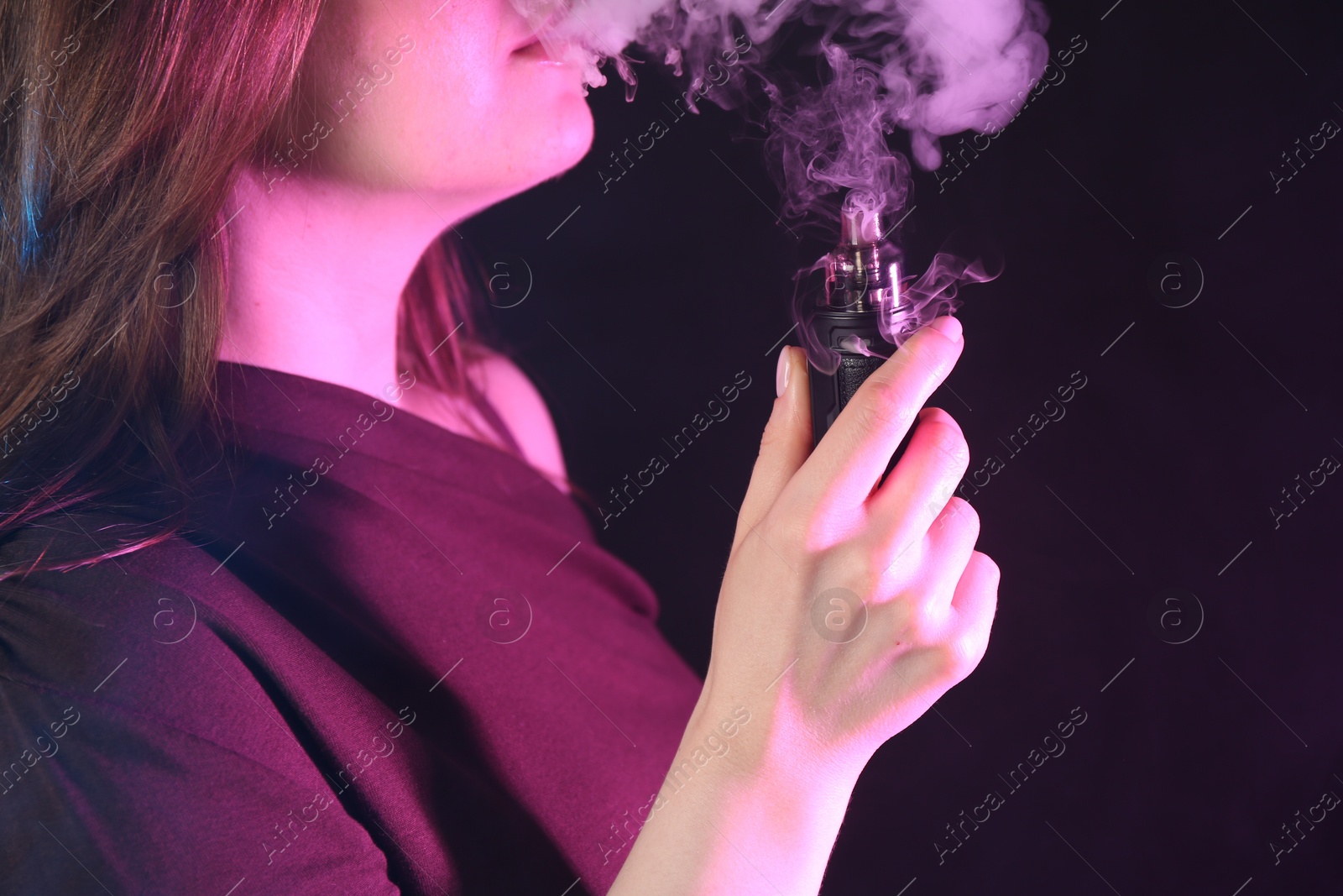 Photo of Woman using electronic smoking device in neon lights on black background, closeup