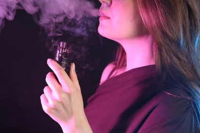 Photo of Woman using electronic smoking device in neon lights on black background, closeup