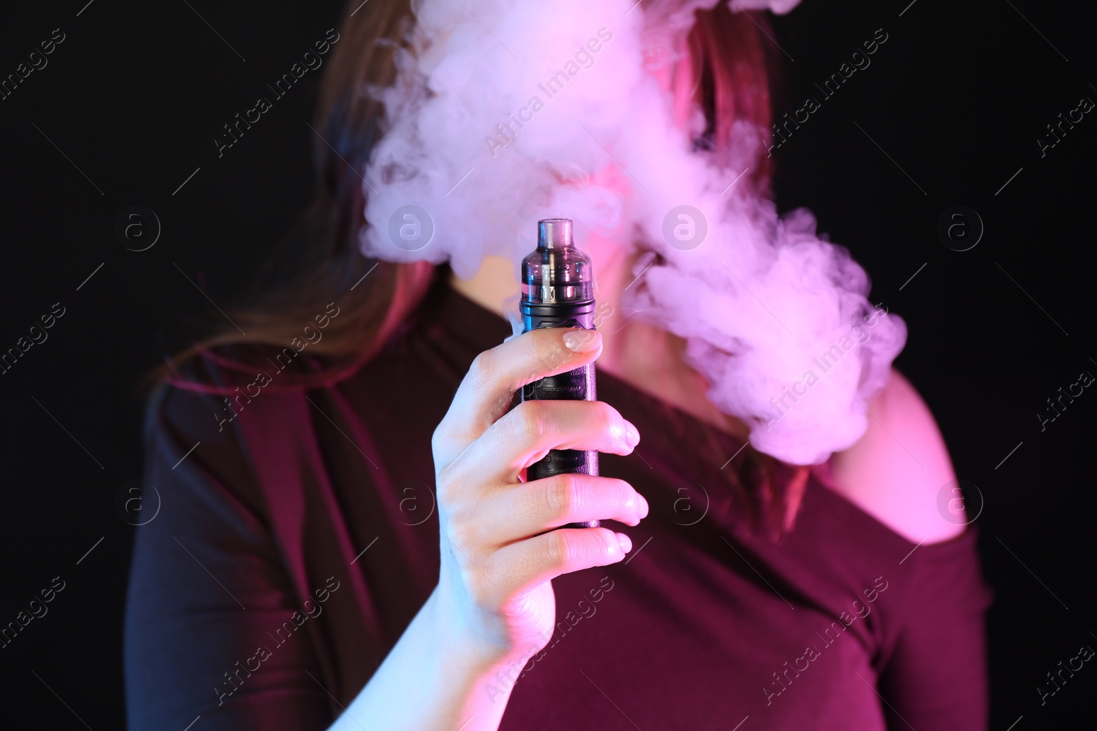 Woman using electronic smoking device in neon lights on black background, closeup Photo of Woman using electronic smoking device in neon lights on black background, closeup