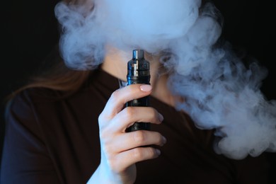 Photo of Woman using electronic smoking device on black background, closeup