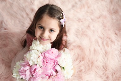 Photo of Cute little girl with bouquet of beautiful peonies on faux fur indoors, above view. Space for text