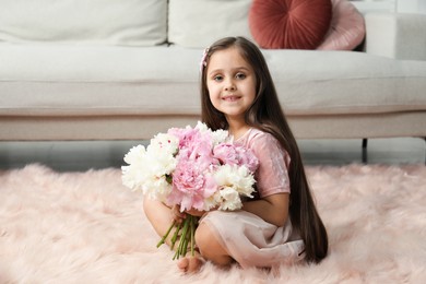 Photo of Cute little girl with bouquet of beautiful peonies on floor at home