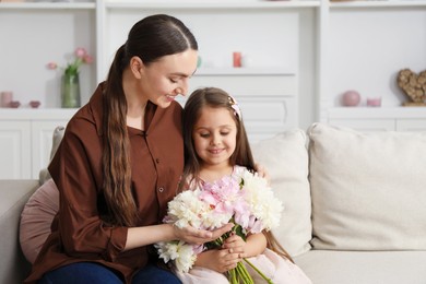 Photo of Mother and her daughter with bouquet of beautiful peonies on sofa at home