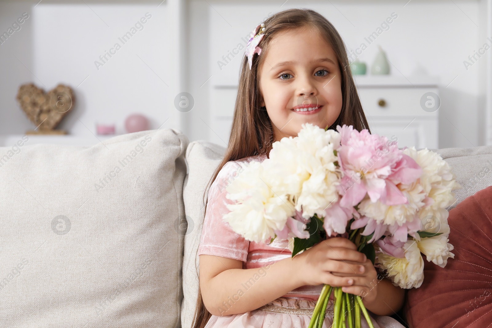 Cute little girl with bouquet of beautiful peonies on sofa at home Photo of Cute little girl with bouquet of beautiful peonies on sofa at home