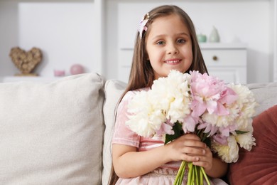 Photo of Cute little girl with bouquet of beautiful peonies on sofa at home