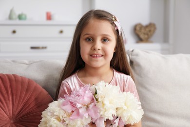 Photo of Cute little girl with bouquet of beautiful peonies on sofa at home