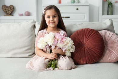Photo of Cute little girl with bouquet of beautiful peonies on sofa at home