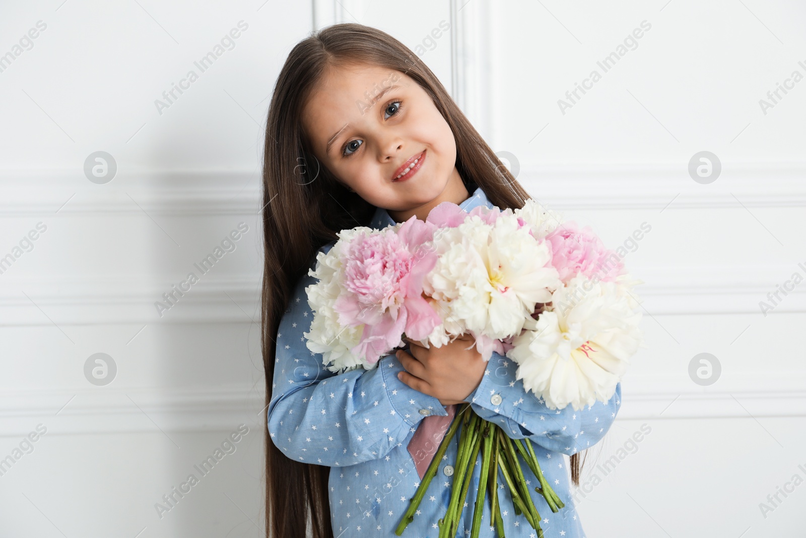 Cute little girl with bouquet of beautiful peonies near white wall indoors Photo of Cute little girl with bouquet of beautiful peonies near white wall indoors