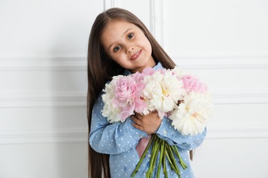 Photo of Cute little girl with bouquet of beautiful peonies near white wall indoors