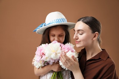 Photo of Mother and her daughter with bouquet of beautiful peonies on brown background, space for text