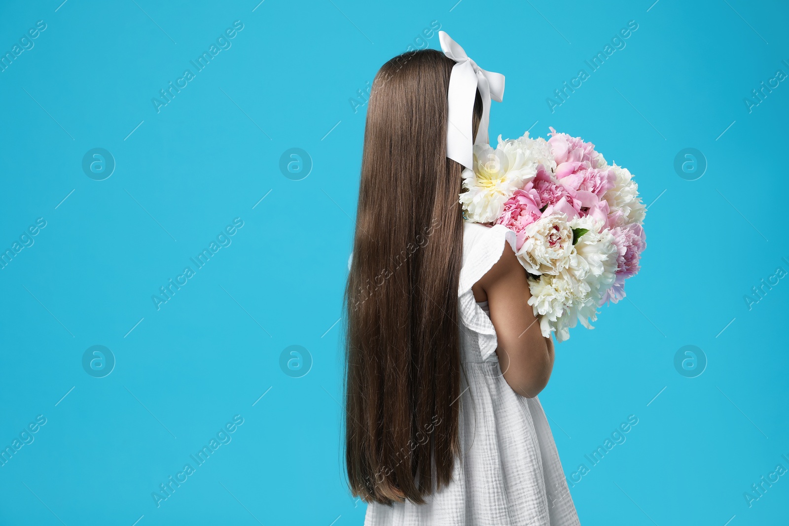 Little girl with bouquet of beautiful peonies on light blue background, back view. Space for text Photo of Little girl with bouquet of beautiful peonies on light blue background, back view. Space for text