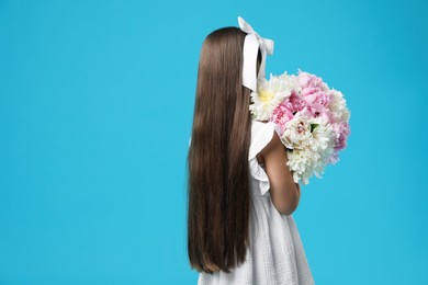 Photo of Little girl with bouquet of beautiful peonies on light blue background, back view. Space for text