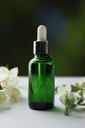 Photo of Essential oil and jasmine flowers on white table against blurred background, closeup