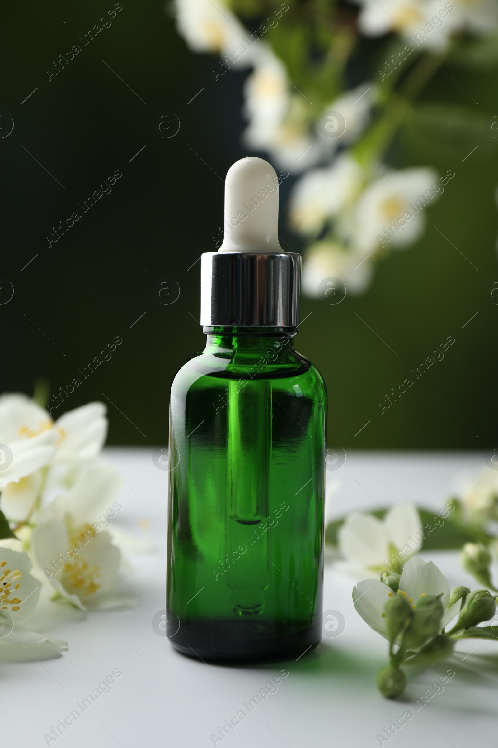 Essential oil and jasmine flowers on white table against blurred background, closeup Photo of Essential oil and jasmine flowers on white table against blurred background, closeup