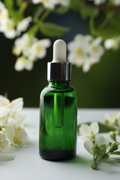 Photo of Essential oil and jasmine flowers on white table against blurred background, closeup