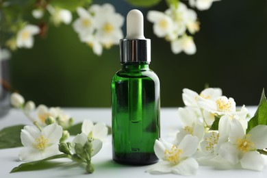 Photo of Essential oil and jasmine flowers on white table against blurred background, closeup