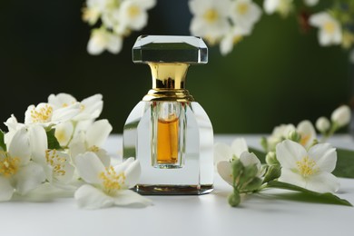 Photo of Bottle of perfume and jasmine flowers on white table against blurred background, closeup