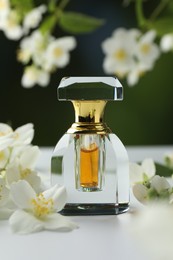 Photo of Bottle of perfume and jasmine flowers on white table against blurred background, closeup