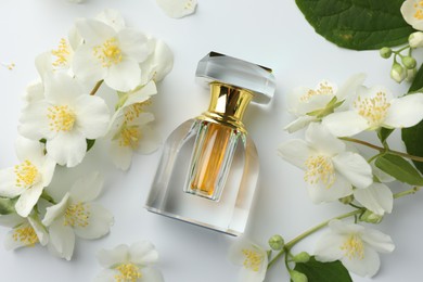 Photo of Bottle of perfume, jasmine flowers and green leaves on white background, flat lay