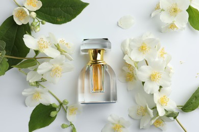 Photo of Bottle of perfume, jasmine flowers and green leaves on white background, flat lay