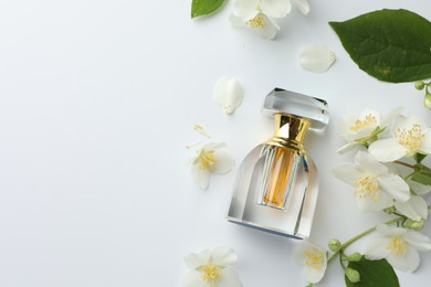 Photo of Bottle of perfume, jasmine flowers and green leaves on white background, flat lay. Space for text