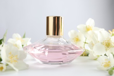 Photo of Bottle of perfume and jasmine flowers on white table, closeup