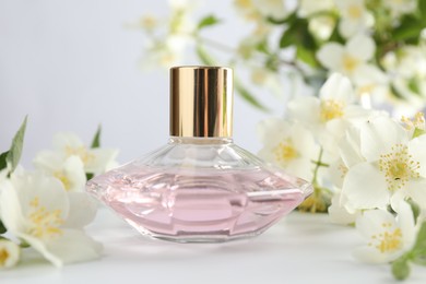 Photo of Bottle of perfume and jasmine flowers on white table, closeup