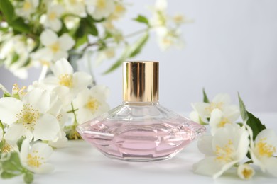 Photo of Bottle of perfume and jasmine flowers on white table, closeup