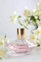 Photo of Bottle of perfume and jasmine flowers on white table, closeup