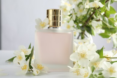 Photo of Bottle of perfume and jasmine flowers on white table, closeup