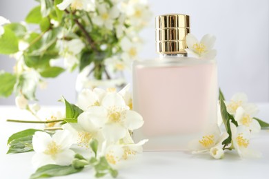 Photo of Bottle of perfume and jasmine flowers on white table, closeup