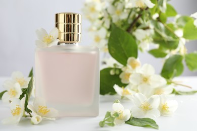 Photo of Bottle of perfume and jasmine flowers on white table, closeup
