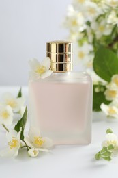 Photo of Bottle of perfume and jasmine flowers on white table, closeup